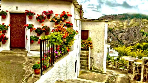 A narrow street with a white building, a red door, and potted plants on the walls. - Nice House in Busquistar (Busquístar)