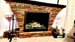 A brick fireplace with a mantel, a basket on top, and a fire burning inside. - Nice House in Busquistar (Busquístar)