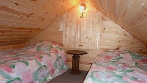 A small, cozy attic bedroom with two single beds, a small table, and a wall-mounted light fixture.