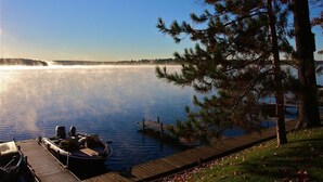 A calm lake with a dock and a boat, surrounded by trees and a clear sky.