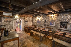 Ein rustikales Interieur mit Steinwänden, Holztischen und Bänken, mit einem Steinkamin und verschiedenen Weinflaschen.