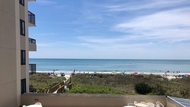 Varanda com vista para a praia, área de estar externa e placa de 'Não Fumar'.
