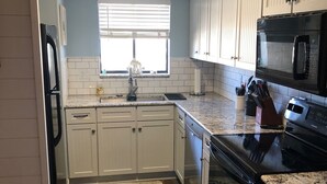 Uma cozinha com armários brancos, fogão preto, micro-ondas e pia.