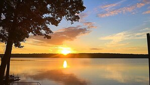 A serene lakeside view at sunset with a dock and a tree in the foreground.