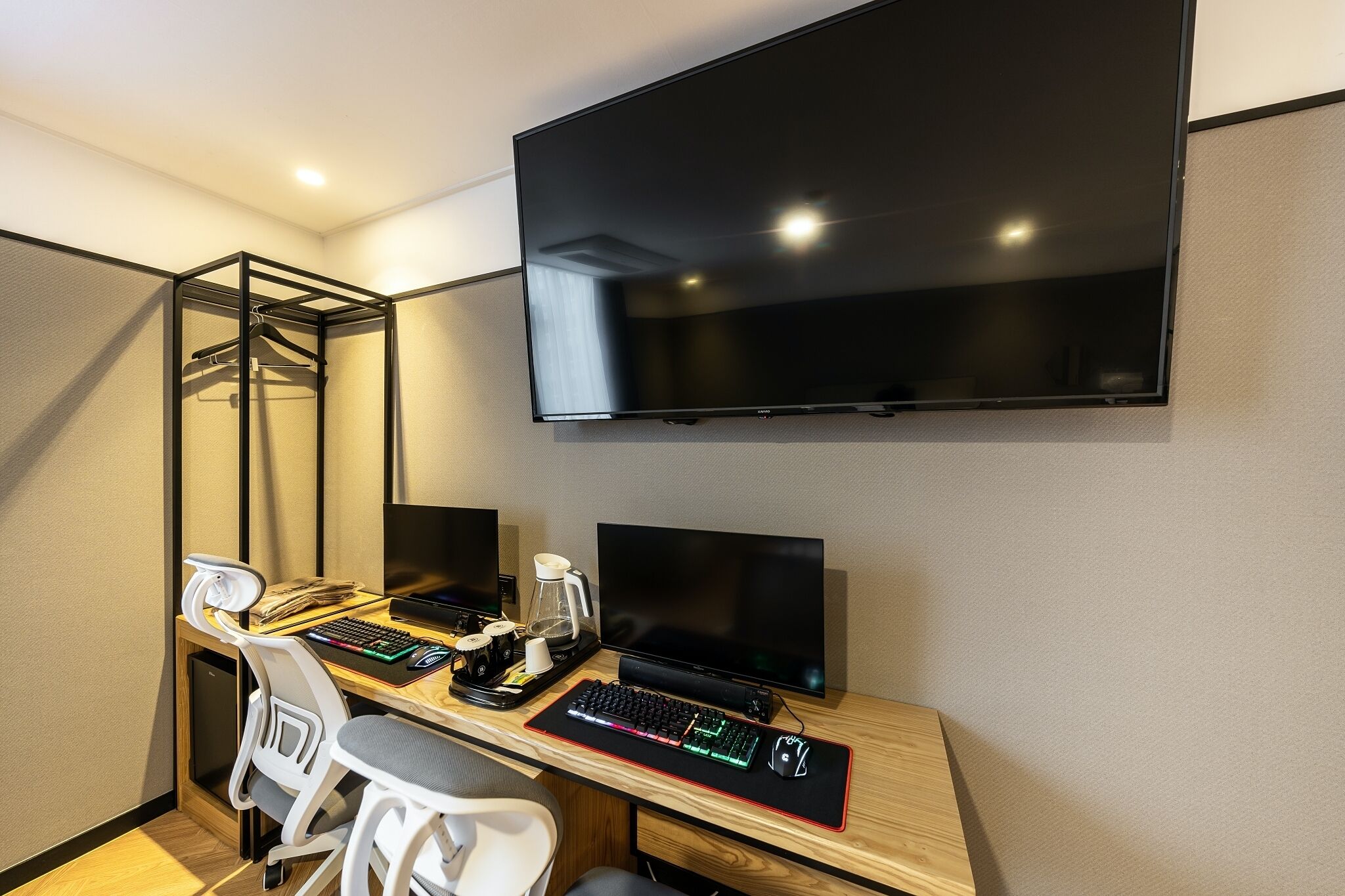 Habitació d'hotel moderna amb un gran televisor de pantalla plana penjat a la paret, una taula de treball amb un ordinador que inclou teclat i ratolí, i una cadira.