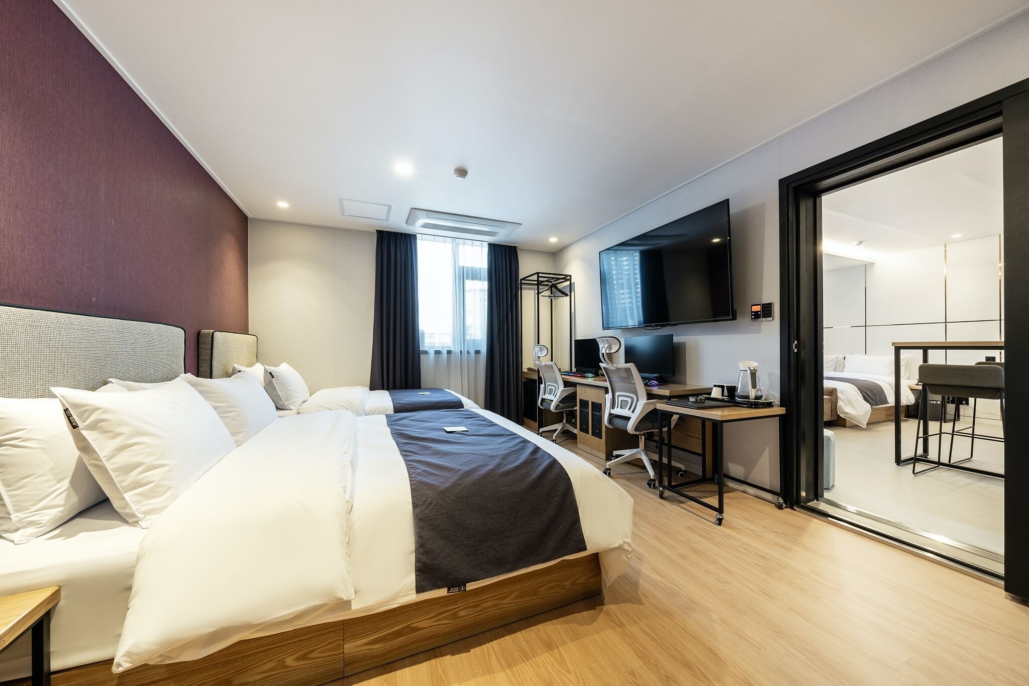 Une chambre d’hôtel avec un grand lit, un bureau avec un ordinateur, une télévision et une porte coulissante donnant sur un balcon.