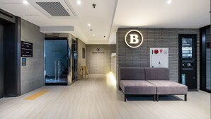 A modern hotel lobby with a reception desk, a seating area, and a staircase leading to the upper floors.