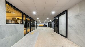 A corridor with glass doors leading to a car parked inside, a tiled floor, and a ceiling with recessed lighting.