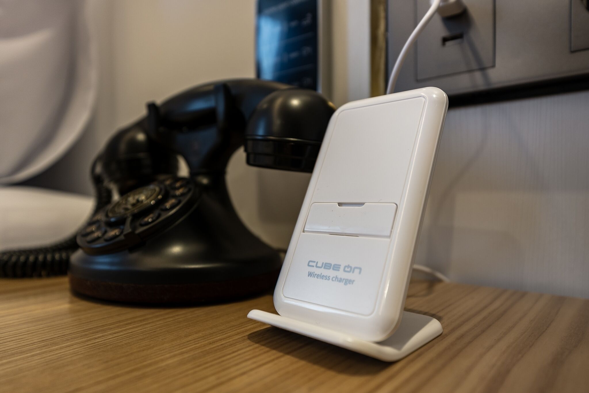 A white wireless charger labeled 'CUBE ON' on a wooden surface next to a black rotary phone.