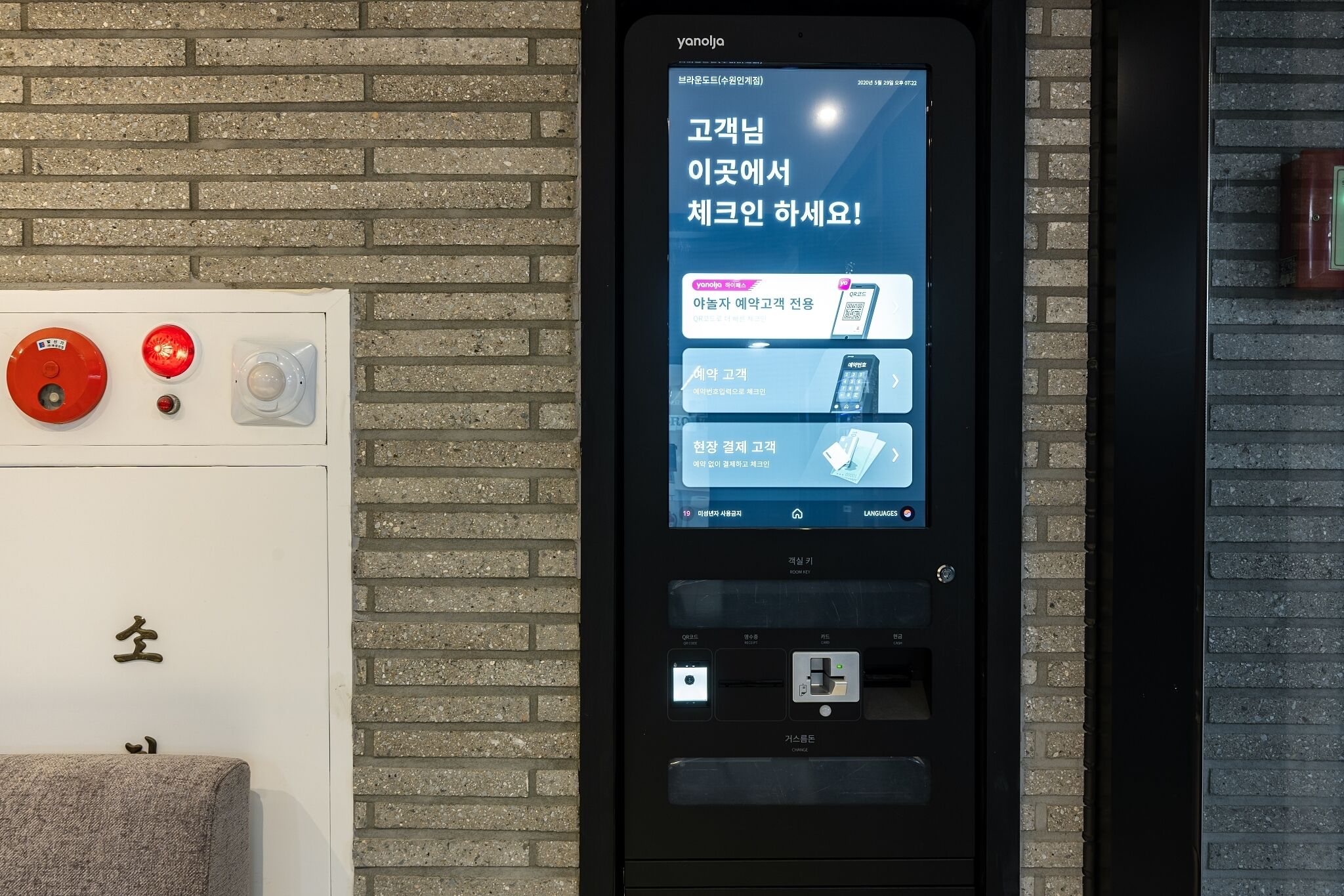A digital kiosk with a screen displaying text in Korean, a red emergency button, and a small camera.