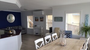 A modern kitchen with white cabinetry, a wooden dining table with white chairs, and a kitchen island with a sink and a bowl.
