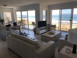 Un saló modern amb sofà, taula de centre, televisió i un balcó amb vista a la platja i l'oceà.