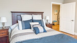A neatly made bed with a patterned bedspread and pillows, a wooden headboard, bedside lamps, and a white door. - Downtown Getaway (Caseville)