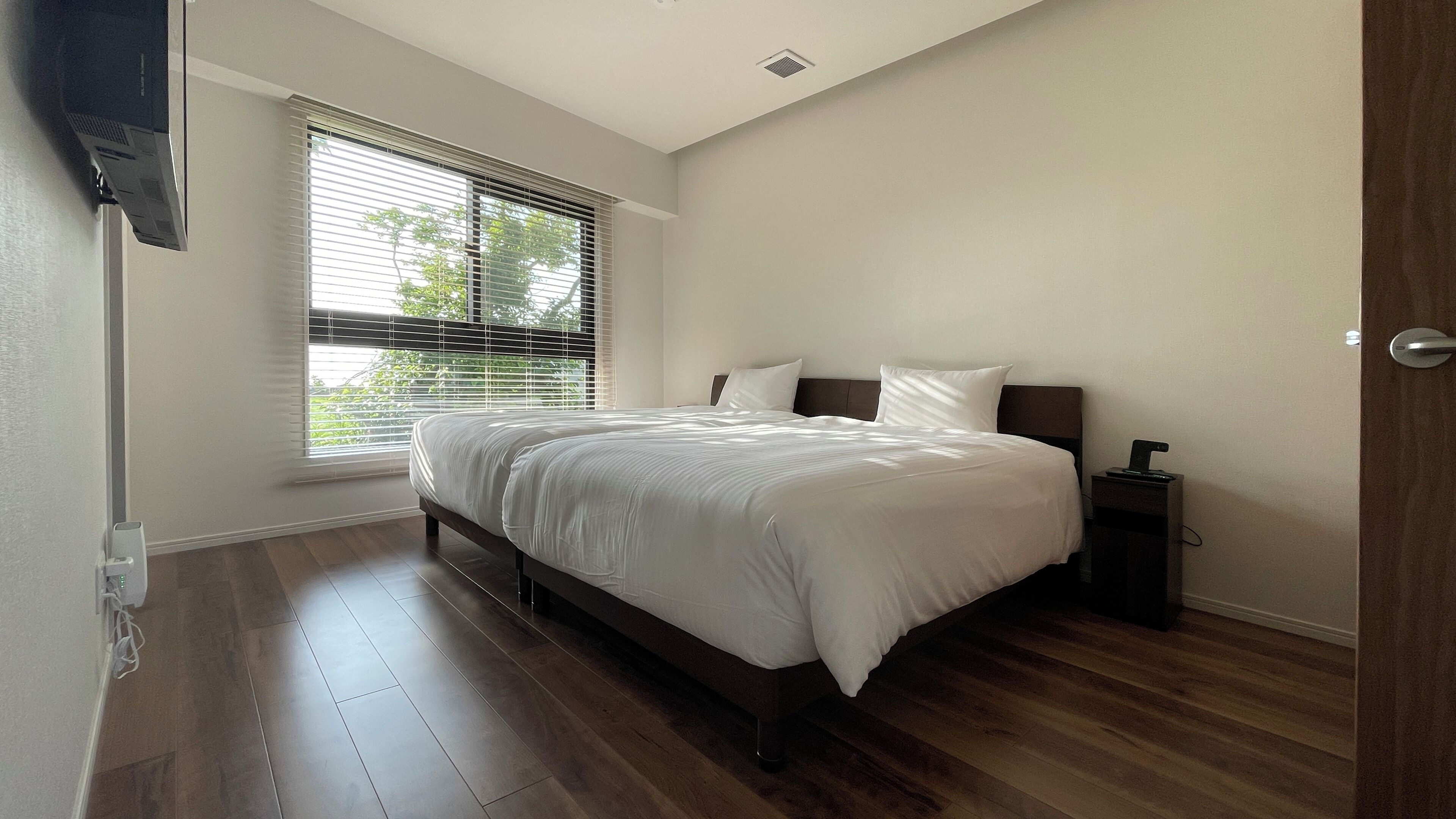 Quarto com cama, mesa de cabeceira, televisão e janela com persianas.