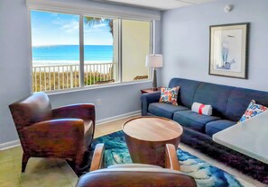 A living room with a view of the beach, a sofa, two armchairs, a coffee table, and a lamp.