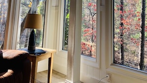 Quarto com janelas amplas, uma luminária, uma mesa e uma cadeira.