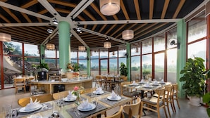 Un restaurante con techo alto, amplios ventanales y una isla central con equipos de cocina.