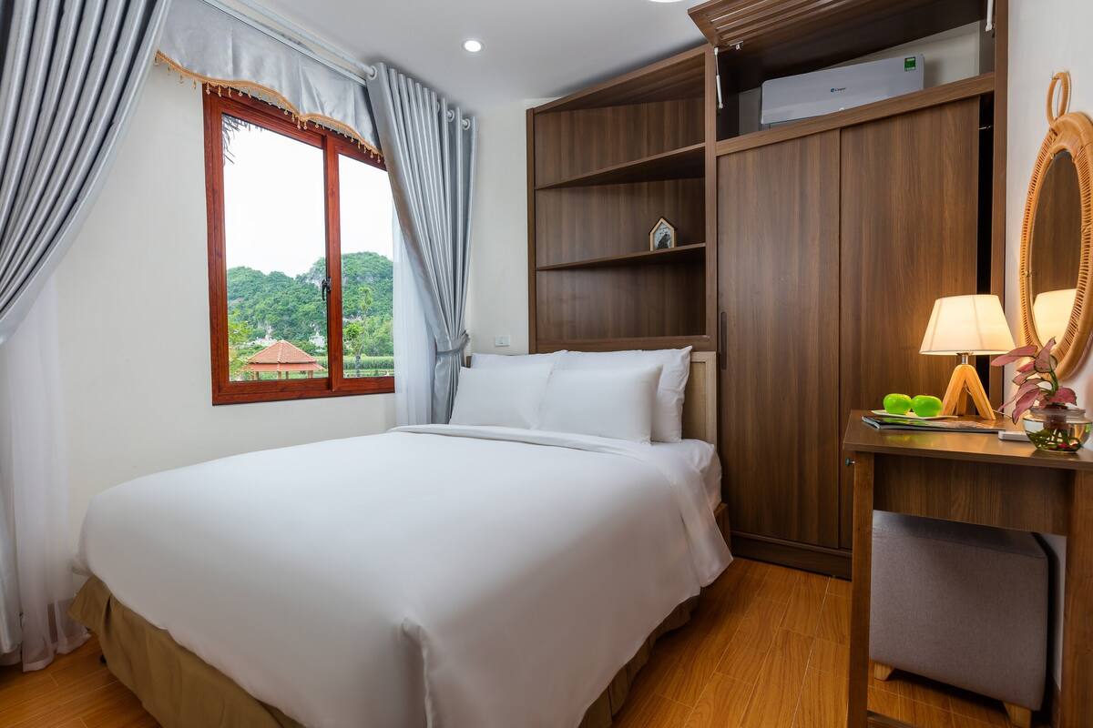 Ein Hotelzimmer mit Bett, Schreibtisch mit Lampe, Spiegel und Kleiderschrank.