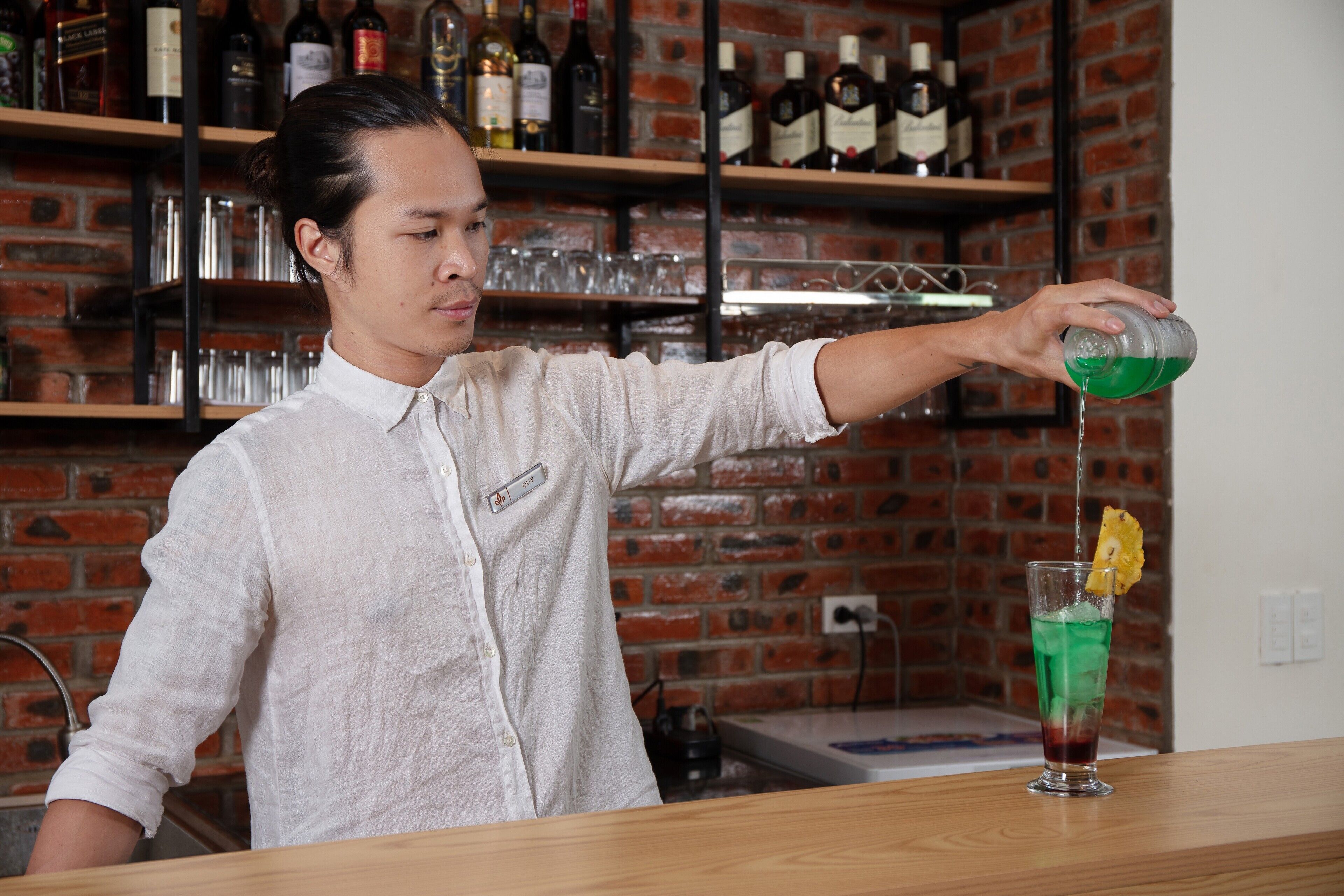 En bartender häller upp en drink i ett glas och lägger i en limeskiva.