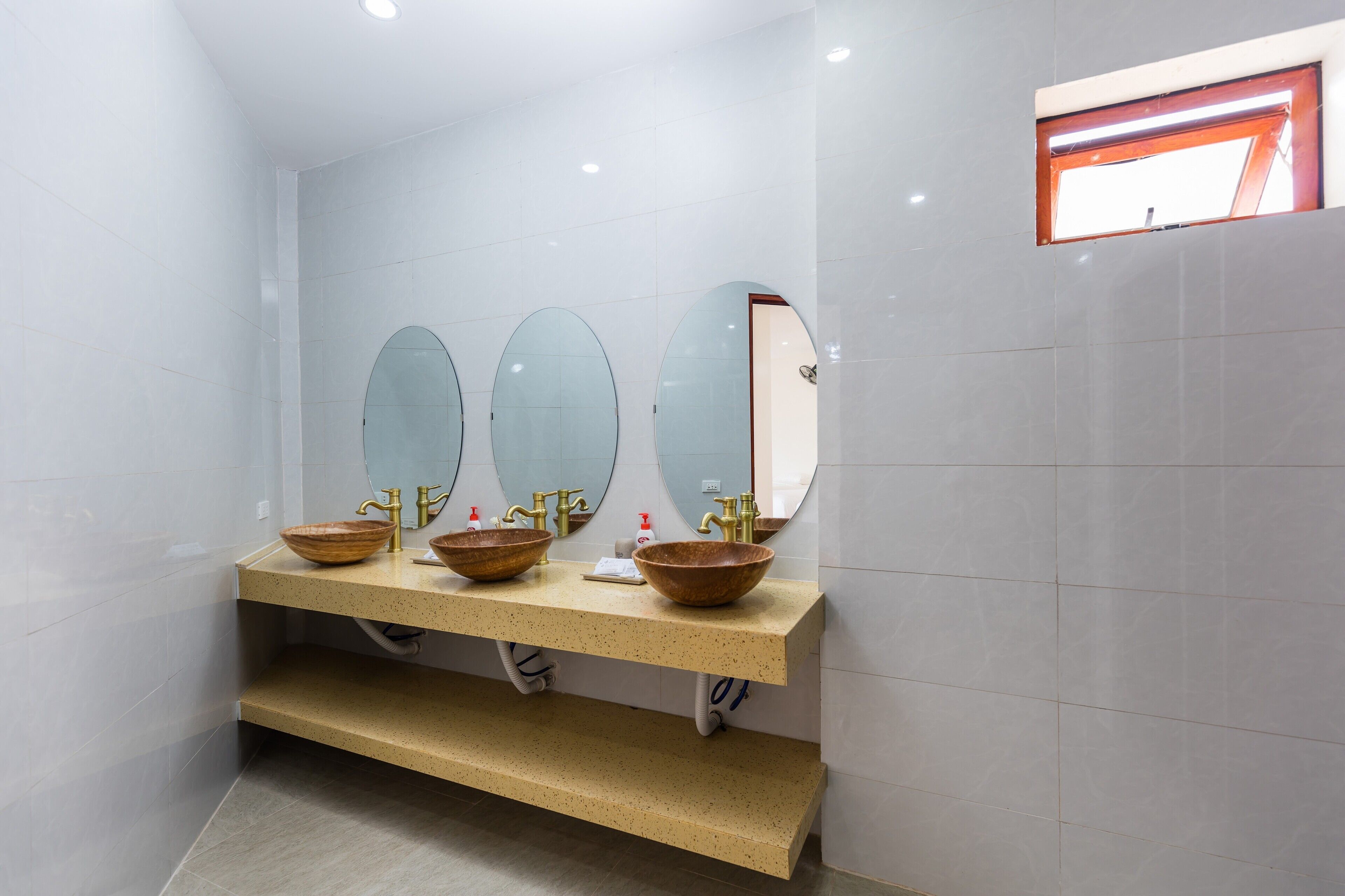 Un baño moderno con tres lavamanos, cada uno con un espejo ovalado grande y un lavabo de madera.