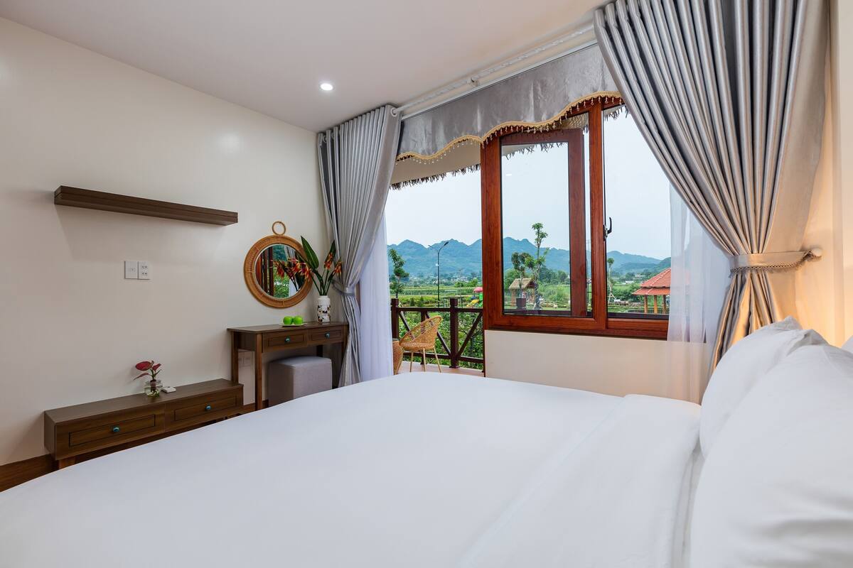 Ein Schlafzimmer mit Bett, Kommode, Spiegel und einem Fenster mit Bergblick.
