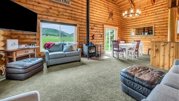 A log cabin interior with a fireplace, a sofa, a television, and a dining area. - Spacious Beautiful Log Cabin Accessible Year Round (Scofield)
