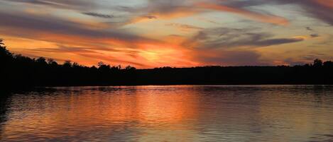A sunset over a calm lake with a silhouette of trees in the background.