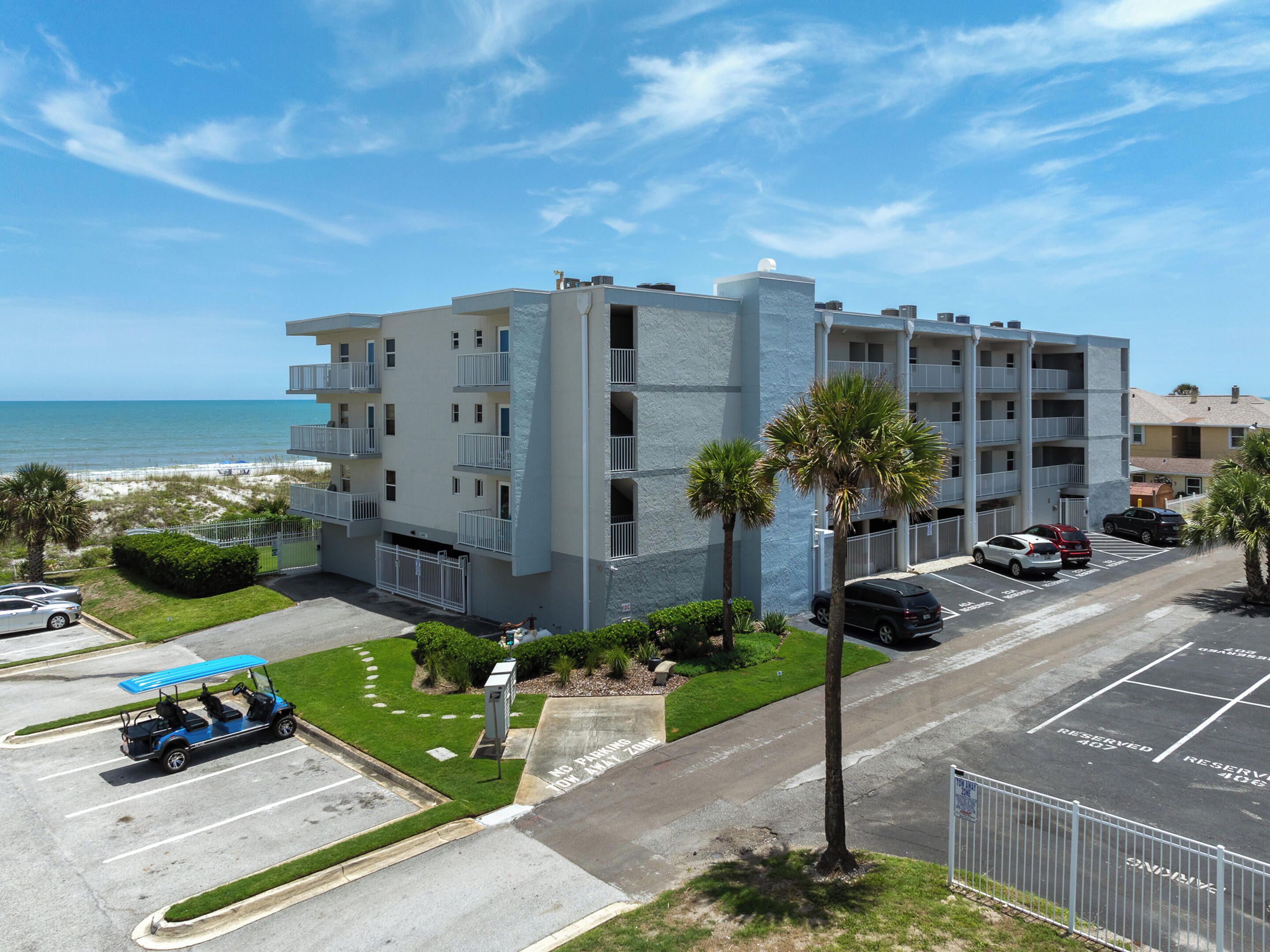 Un edificio de varios pisos con estacionamiento, un carrito de golf y vistas a la playa.