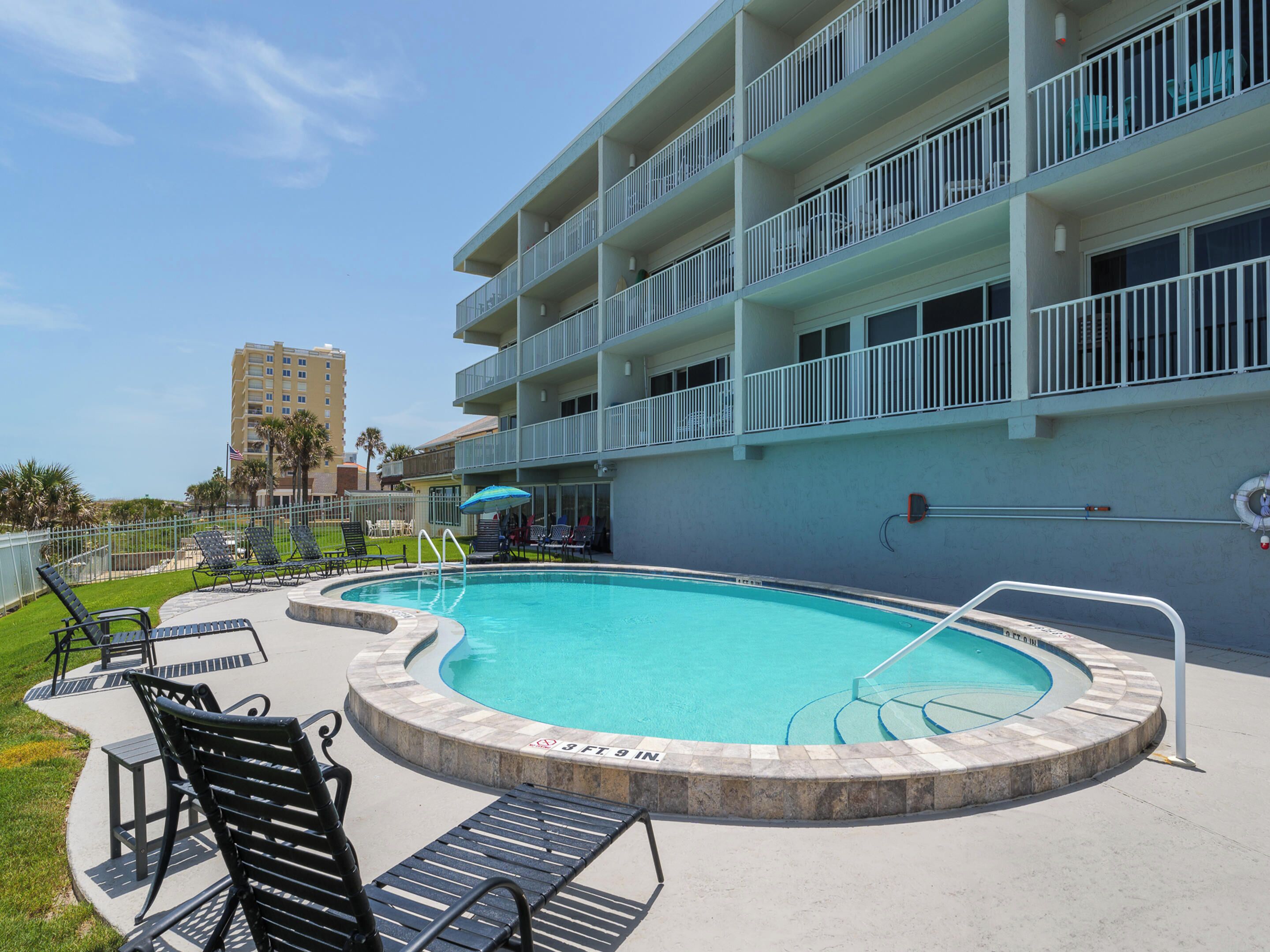 A swimming pool with a curved edge, surrounded by lounge chairs and a poolside area.