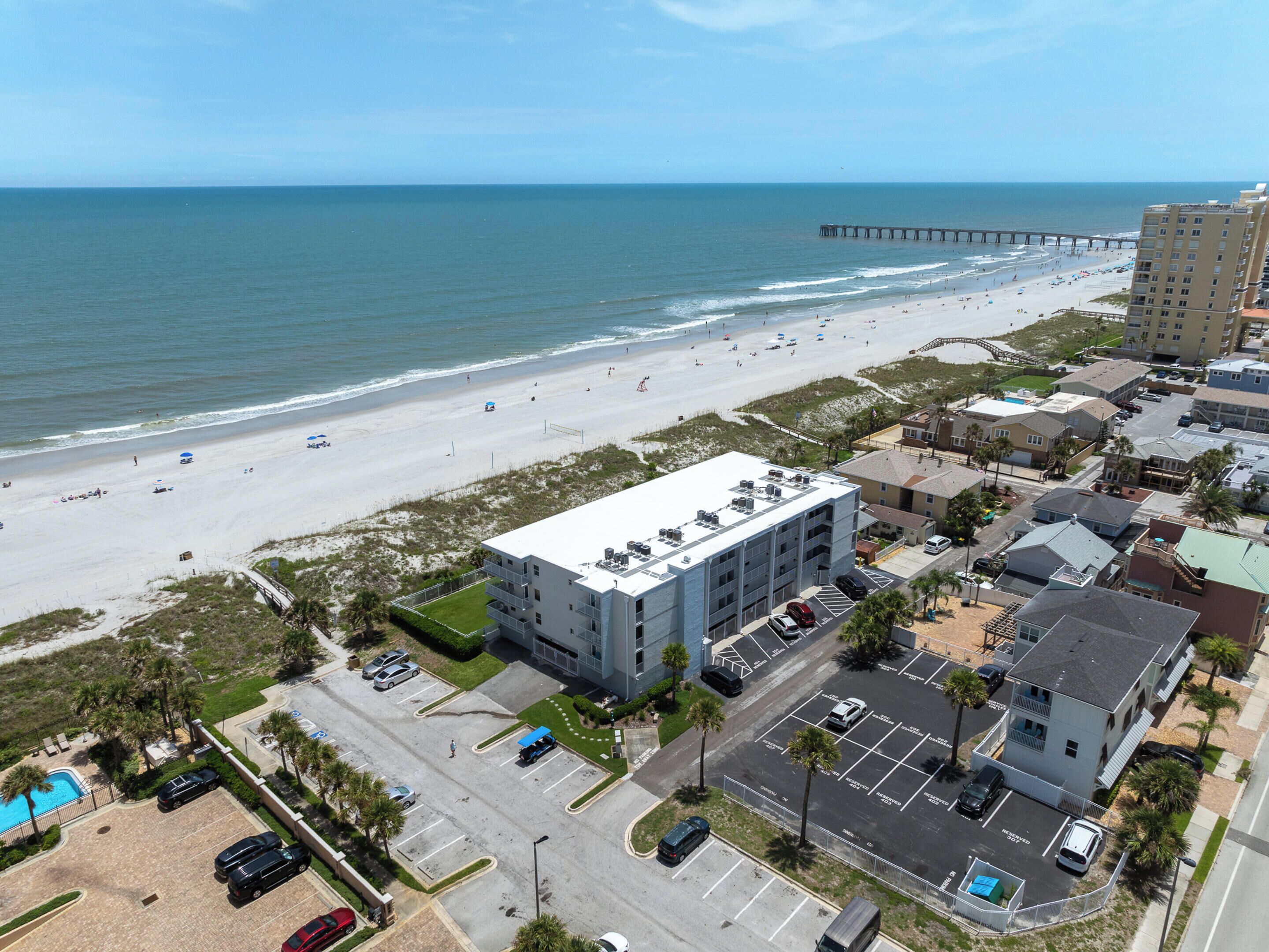 Un hôtel situé sur la côte, doté d’un parking, offrant une vue sur la plage et avec une jetée en arrière-plan.