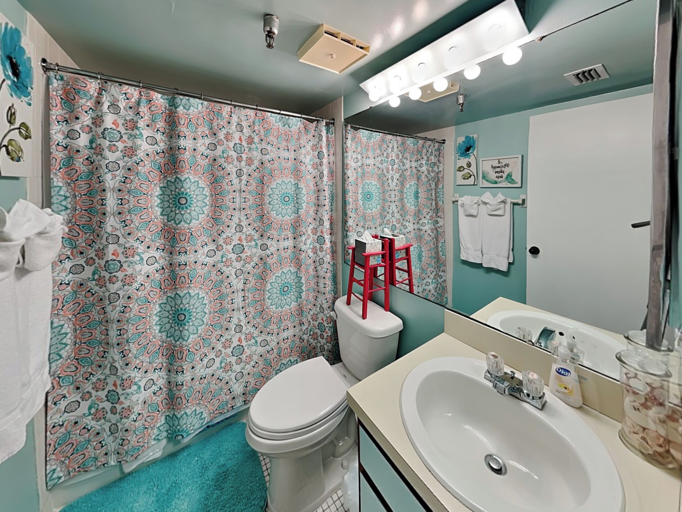 A bathroom with a patterned shower curtain, a white toilet, a sink with toiletries, and a mirror.