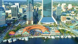 A cityscape with modern skyscrapers, including a prominent 'modis' building, a waterfront area with boats, and a large curved building with a red roof. - Jacksonville Beachdrifter by Distinctive Beach Rentals (Jacksonville Beach)