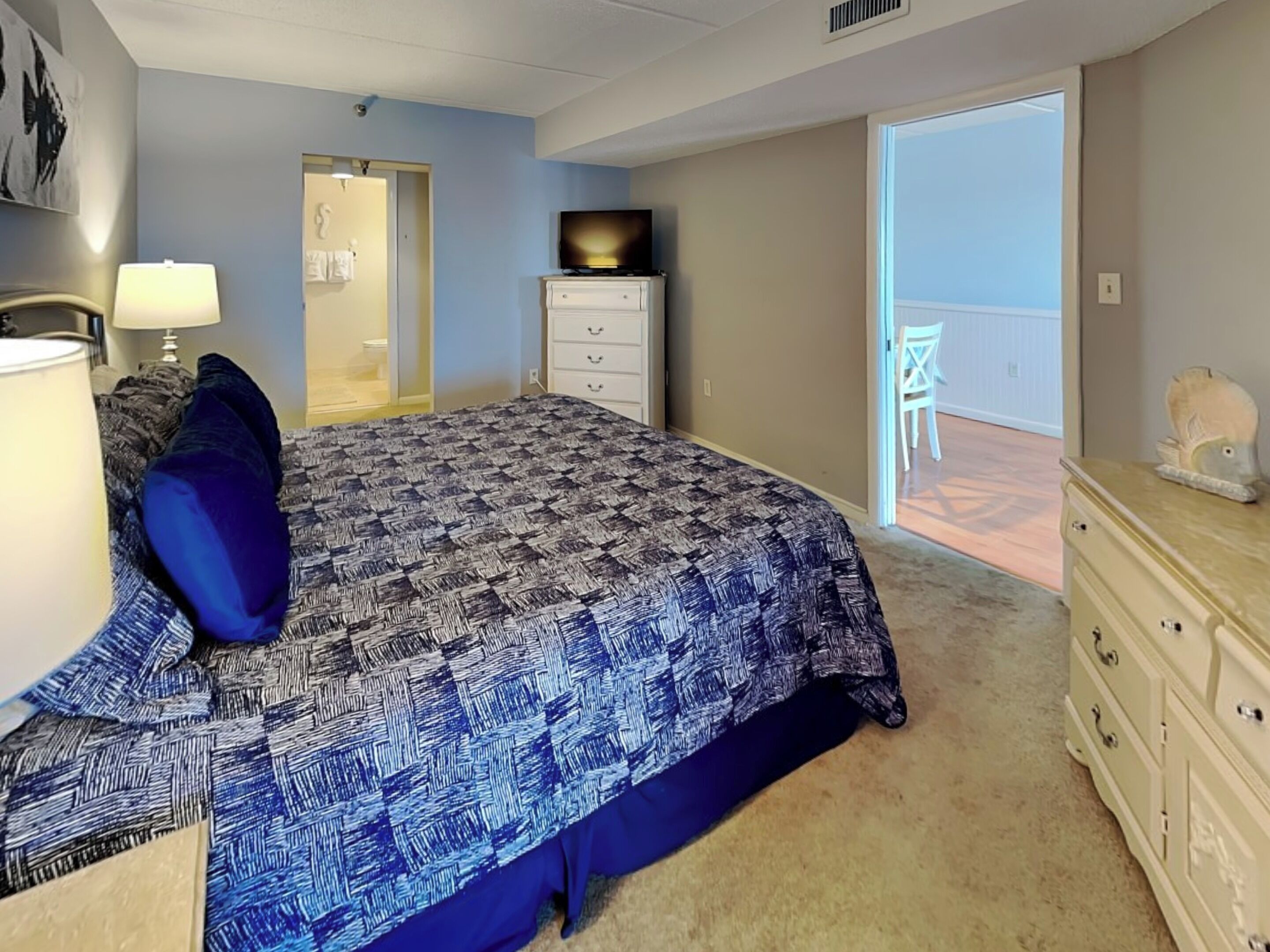 A bedroom with a bed, dresser, and a door leading to a balcony.