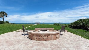 A paved pathway leading to a circular seating area with a fire pit, overlooking a beach. - Seashell by Distinctive Beach Rentals (Ponte Vedra Beach)