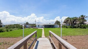 A wooden pathway leading to a building with a large window and a covered porch area. - Seashell by Distinctive Beach Rentals (Ponte Vedra Beach)