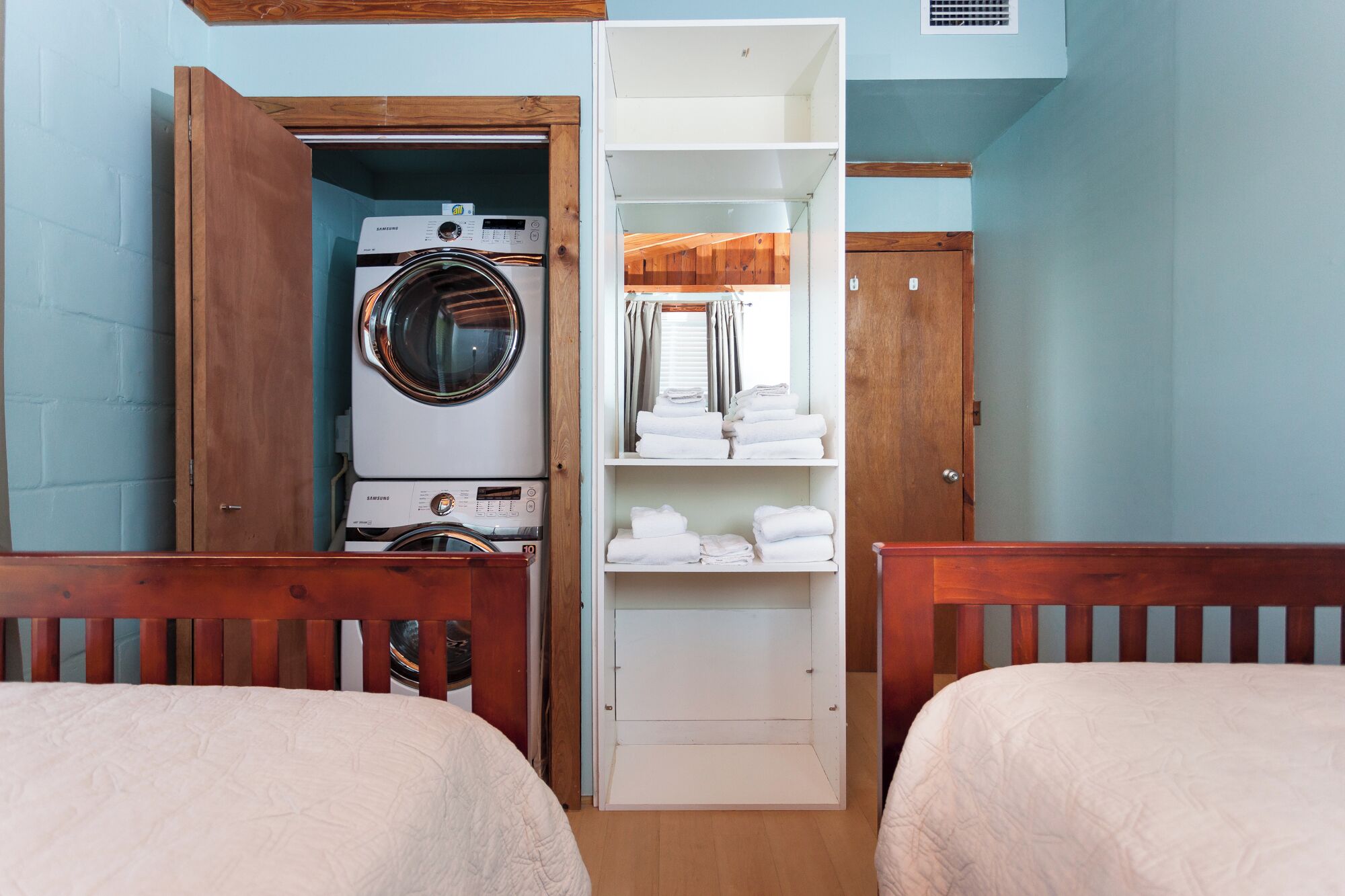 Een slaapkamer met twee houten bedden, een wasmachine en een witte plank met opgevouwen handdoeken.