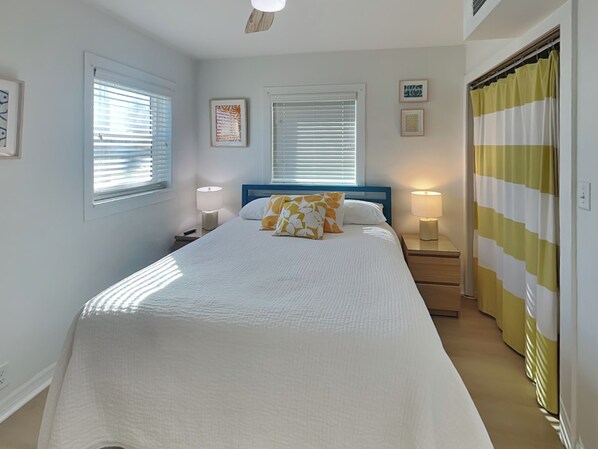 Un dormitorio ordenado con una cama grande, dos mesitas de noche con lámparas y una ventana con persianas.