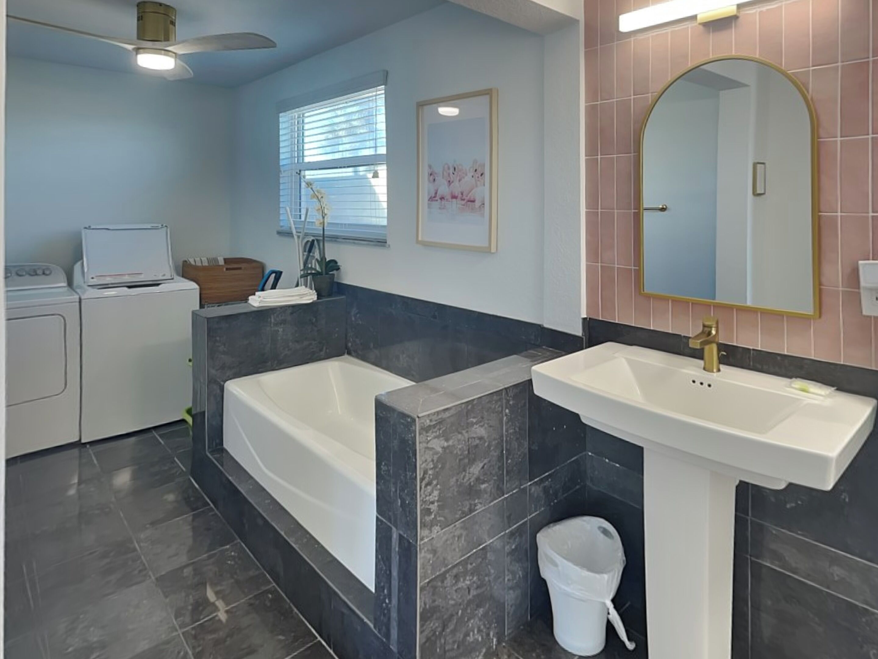 Une salle de bain moderne dot ée d’une douche à deux pommes de douche et d’un double lavabo, d’un ventilateur de plafond et d’un espace buanderie.