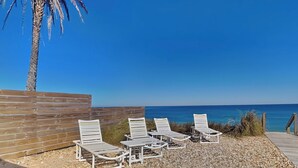 Un área de descanso en la playa con cuatro sillones blancos y una palmera.