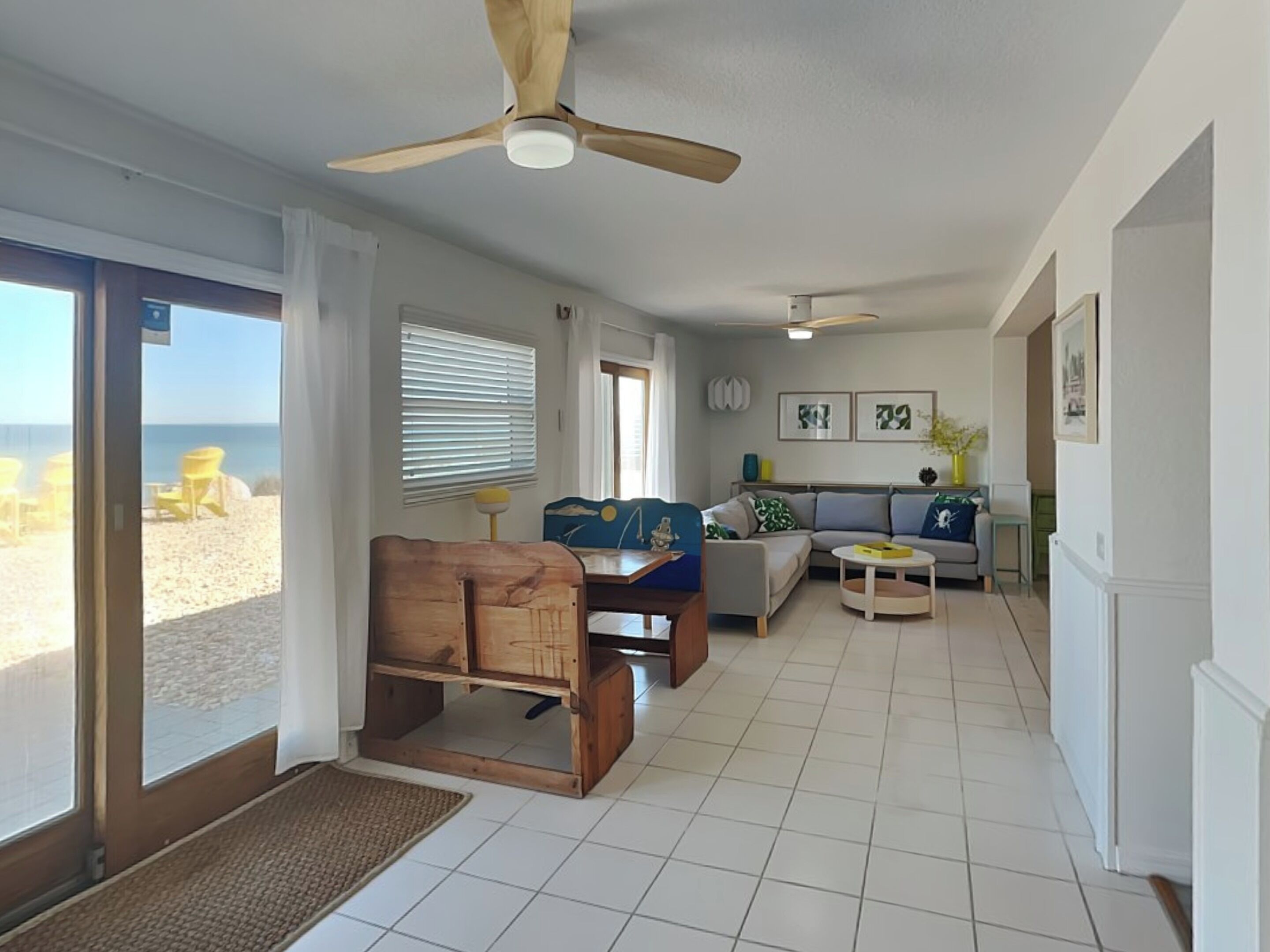 A spacious living room with a ceiling fan, a sofa, a coffee table, and a view of the beach through large windows.