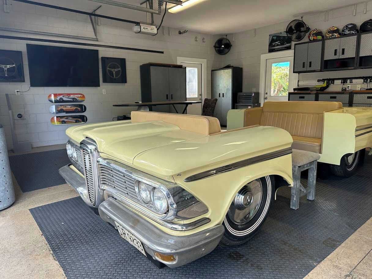 Ein Oldtimer in einer Garage mit Werkbank, Schränken und Helmen an der Wand.