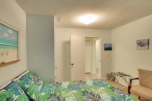 Een slaapkamer met een bed, een stoel, een deur die naar een andere kamer leidt en een plafondlamp.