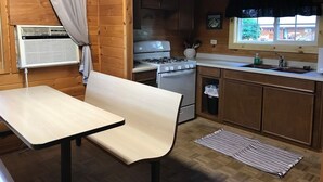 A compact kitchen with a stove, oven, and sink. There is a small table and a bench.