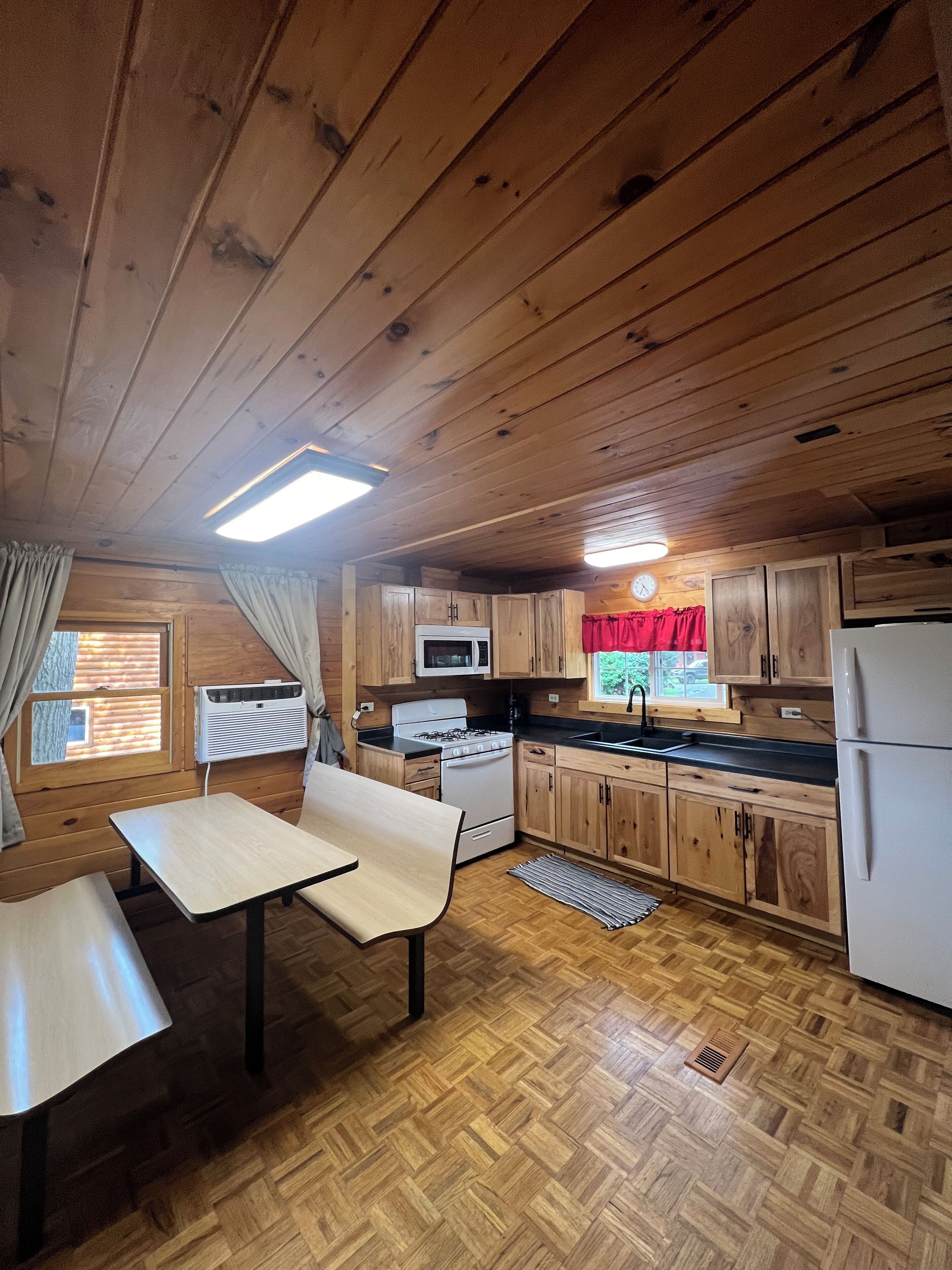 Une cuisine rustique aménagée dans une cabane en bois, avec une table à manger, un fourneau, un four à micro-ondes et un réfrigérateur.