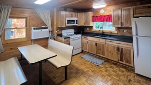 A wooden cabin kitchen with a dining table, a stove, a microwave, and a refrigerator.