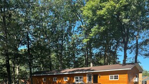 A log cabin with a deck and a picnic table, surrounded by trees.