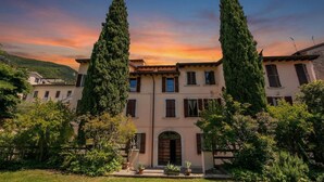 A building with a symmetrical facade, tall cypress trees, and a well-maintained garden. - Berny Salò: Near the Lake & Garage, Apartment, Salò, Italy (Salò)