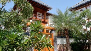 Ein traditionelles Gebäude mit einem hölzernen Balkon, umgeben von üppiger Vegetation und einer Steinmauer.