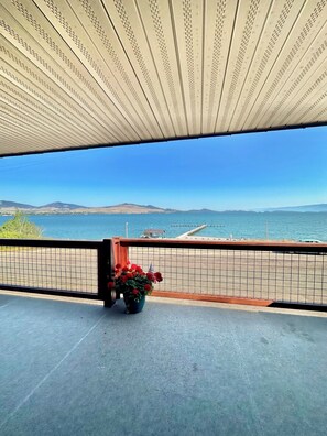 Un balcon avec vue sur la mer, une jetée et des collines lointaines.