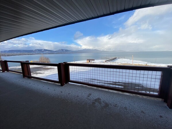Enjoy the serene views of the surrounding water and mountains from this outdoor viewing area with a grid-patterned railing and a pier in the distance.